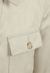 Lichtbeige shirt met een zachte, suède-achtige textuur, een klepzak met een ronde, lichtgekleurde knop en net afgewerkte randen.