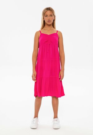 Fuchsia mouwloze jurk met geplooide voorkant en gelaagde rok. Gemaakt van lichtgewicht stof, gecombineerd met witte sneakers voor contrast.