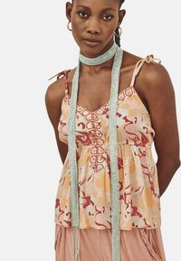 Top sin mangas de estampado floral en tonos durazno con un cuerpo fruncido, escote detallado y tirantes finos. Presenta un acento texturizado.