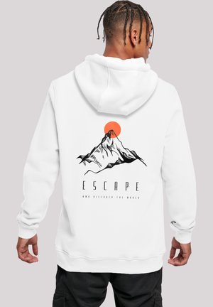 Person with braided hair wearing a white hoodie with a mountain and orange sun graphic and the word "ESCAPE" on the back.