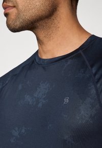 Tengerészkék sportos póló texturált mintával, kerek nyakkivágással és rövid ujjal. A mellrészen kis logóval díszítve.