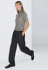 Gray short-sleeve turtleneck top paired with loose black trousers and textured black shoes, set against a minimalist background.