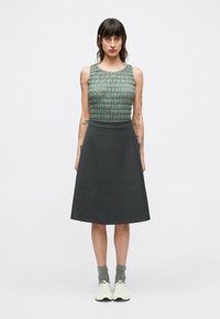 Mouwloos groen topje met gestructureerde details gecombineerd met een donkergrijze A-lijn rok. Model draagt grijze sokken en witte schoenen. Eenvoudig, modern ontwerp.