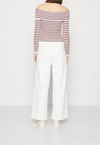 Top off-the-shoulder a righe rosse e bianche abbinato a pantaloni bianchi a gamba larga. Tessuto morbido e leggero. Accenti di sneaker casual.