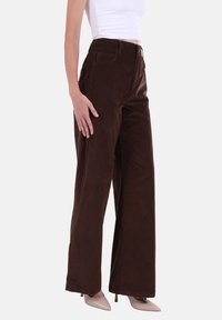 Pantaloni a gamba larga in velluto a coste marrone con vita alta e tasche frontali. La texture morbida e i dettagli di cucitura minimalisti valorizzano il design.