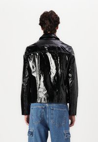 Sorte patentlæderjakke med en blank finish, featuring en klassisk krave og struktureret form, båret over blå denim bukser.