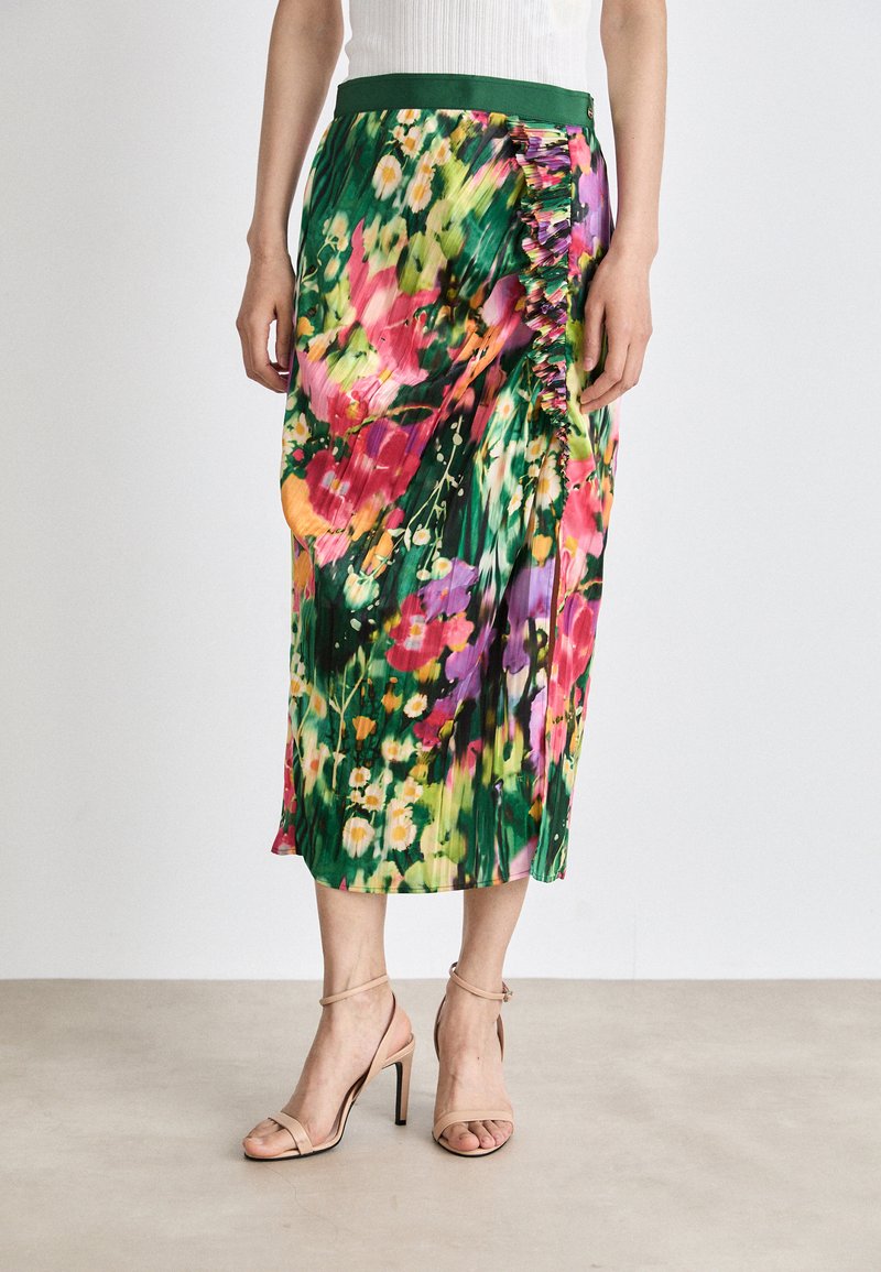 Květinová midi sukně se zeleným pasem, zdobená živými vzory v růžové, žluté a fialové barvě, s volánkovým detailem po jedné straně.