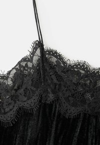 Sort fløjlstøj med tynde stropper og intrikate blomster-lace kant langs udskæringen mod en hvid baggrund.