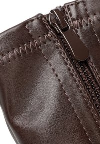 Detailní záběr tmavě hnědé kožené boty s viditelným zipem a ozdobným cikcak stehem podél švu.