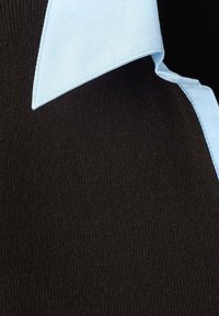 Tissu côtelé noir avec un col de chemise bleu clair. Le col a une texture lisse et des bords finis, contrastant avec les côtes du tissu.