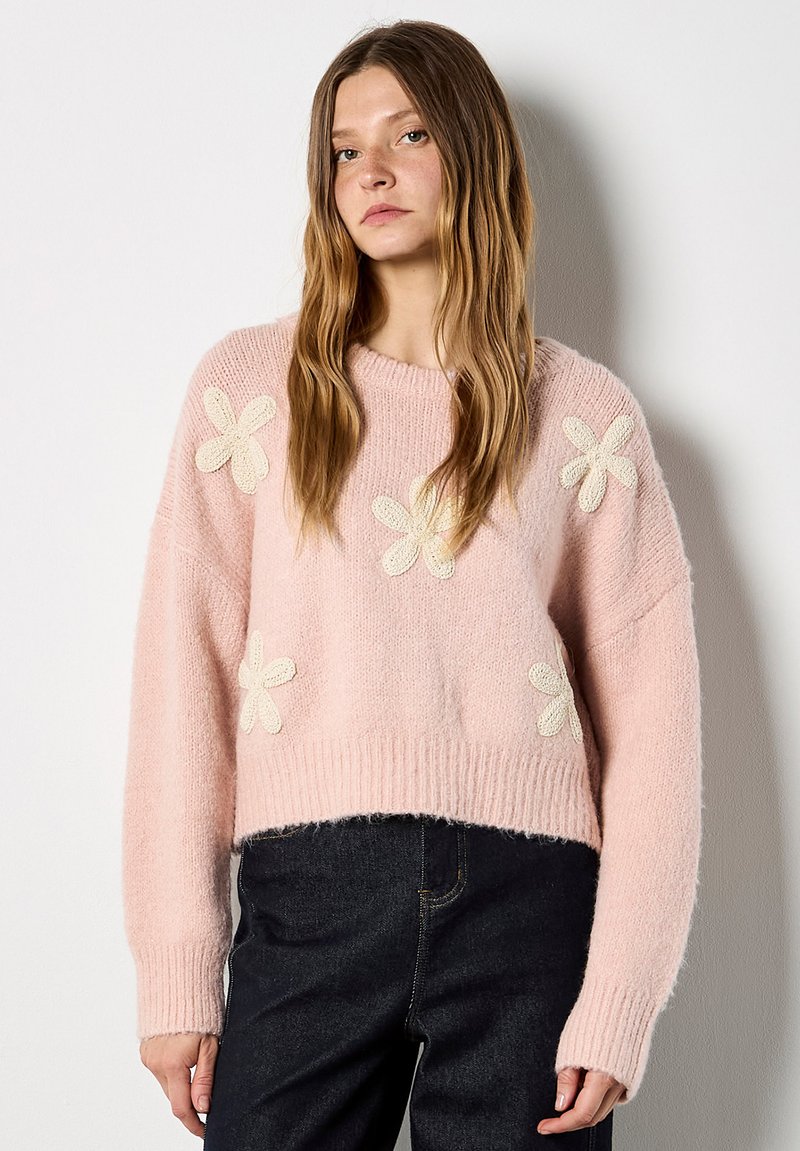 Pull en tricot rose au design court, orné d'appliqués de fleurs crème texturées sur le devant, avec des poignets et un ourlet côtelés.