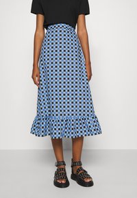 Blaue und schwarze karierte Midirock mit einem Rüschensaum, aus leichtem Material. Kombiniert mit schwarzen, mit Nieten besetzten Sandalen.