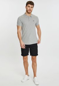 Camisa polo gris con cuello, combinada con pantalones cortos negros enrollados. El modelo lleva zapatillas blancas. Diseño simple, material de algodón.