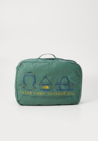 Grønn duffelbag med rutenettmønster, laget av resirkulerte materialer, har glidelås, bærehåndtak og trykt design med flere bærealternativer.