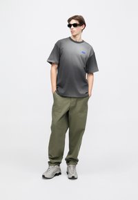 Γκρι γραφικό μπλουζάκι με κοντά μανίκια, μπλε λογότυπο. Χαλαρό παντελόνι σε ελιά χρώμα με πλαϊνές τσέπες. Γκρι αθλητικά παπούτσια με υφασμένο πέλμα και μαύρες λεπτομέρειες.