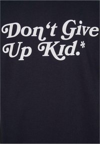 Texte blanc sur tissu noir affichant "Don't Give Up Kid" dans une police à empattement en gras.
