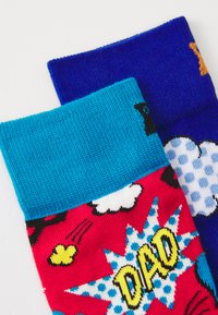 Dois meias: uma com uma base vermelha apresentando texto em estilo de banda desenhada "PAPÁ" e nuvens coloridas, a outra em azul com pequenos pontos e acentos.