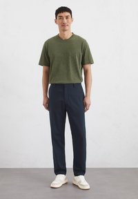 Green striped short-sleeve t-shirt, navy trousers, and white sneakers. Cotton fabric with a relaxed fit. Simple design, no visible patterns.