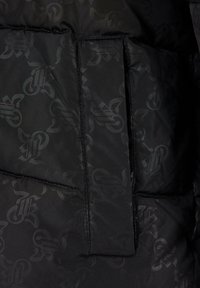 Sort puffers jakke sektion med et struktureret mønster og en solid stoflap. Glat materiale og quiltet design med synlige sømme.