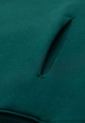 Vihreä kangaspaita, jossa on teksturoitu taskuaukko ja sileä pinta, korostaen sen pehmeyttä ja siistejä linjoja.