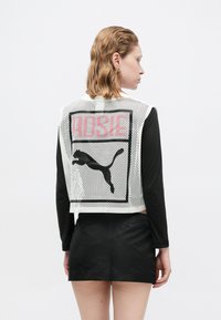 Witte mesh cropped vest met zwarte bies, met een roze "PUSSIE" graphic en een zwart puma logo op de achterkant. Zwarte fitted rok.