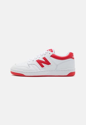 Hvid og rød lav New Balance sneaker med rødt "N"-logo, rød hælkappe og rød gummisål, set fra siden på en ensfarvet baggrund.