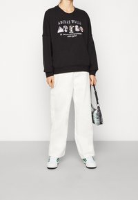 Svart sweatshirt med grafiskt tryck, avslappnad passform, ribbade muddar, ihopparad med vita vida byxor och en liten svart och vit väska.