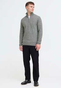 Harmaa neulepusero, jossa on neljännesvetoketju kauluksessa, yhdistettynä mustiin kumpuihin ja mustiin kenkiin, joissa on tekstuurinen kankaan pinta.