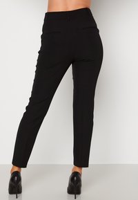 Skräddarsydda svarta byxor med smal passform, med en slät textur, två bakfickor och medelhög midja. Styla med högklackade skor.