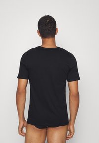 T-shirt noir en coton à manches courtes, avec un col arrondi et une texture lisse, présenté sur une personne vue de dos.