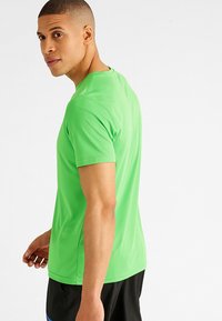 Groene sportt-shirt gemaakt van lichtgewicht stof, met korte mouwen, een ronde halslijn en een gladde textuur. Eenvoudig ontwerp.