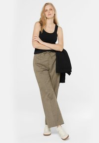 Schwarzes Tanktop, kariert braune weit geschnittene Hose, weiße Sneakers und ein schwarzer Pullover, der über dem Arm hängt. Einfaches Design mit lockerer Passform.