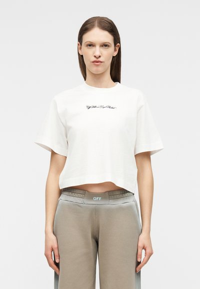 Νεαρή γυναίκα με ίσια καστανά μαλλιά φορά λευκό κοντό μπλουζάκι με κείμενο και γκρι ψηλόμεσα φόρμα με λογότυπο "OFF" στη μέση.