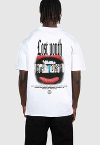 Vit bomull t-shirt med ett grafiskt tryck av röda läppar och en bunt kontanter, med texten "Lost Youth" och ytterligare fraser nedanför.