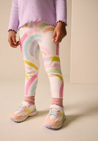 Krāsainas legingas ar abstraktiem varavīksnes rakstiem pasteļtoņos uz baltas ribotas auduma. Kopā ar gaiši rozā un daudzkrāsainām sporta kurpēm.