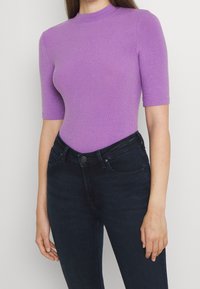 Bodysuit morado de canalé con mangas cortas y cuello alto. Combinado con unos vaqueros azul oscuro de diseño clásico de cinco bolsillos.