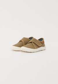 Braune Segeltuchschuhe mit einem Klettverschluss, weißer Gummisohle und einer strukturierten Oberfläche. Auffälliger Lederakzent an der Ferse.