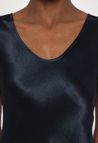 Mørkeblå satintopp med bred V-hals, med en glatt tekstur og minimalistisk design. Stoffet ser noe skinnende og kroppsnært ut.