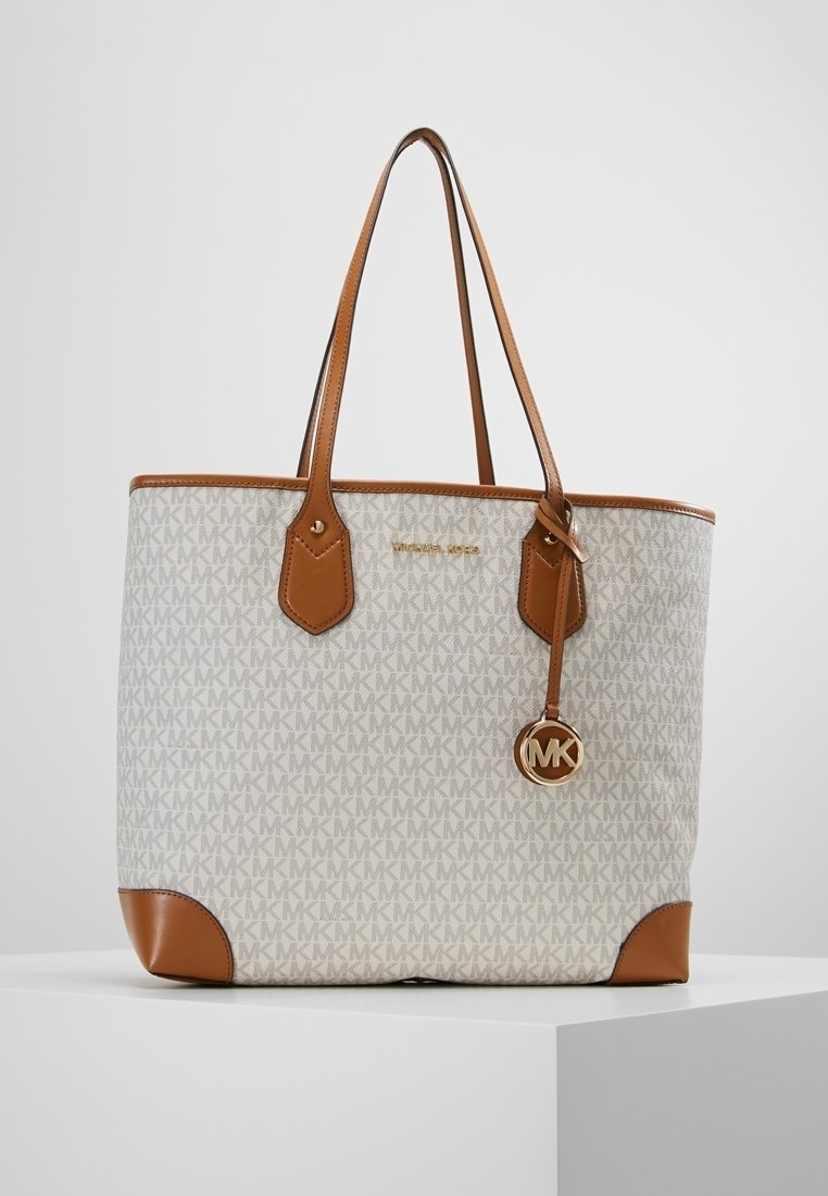 Sac cabas Michael Kors beige et marron avec motif logo MK, poignées en cuir marron, bordure et breloque ronde MK suspendue à une lanière.