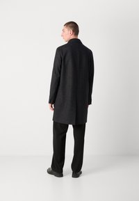 Cappotto lungo grigio scuro realizzato in tessuto texturizzato, con una singola fessura posteriore, collo a punta e polsini con bottoni. Vestibilità slim con tasche laterali.