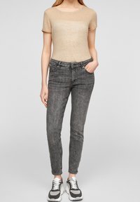 Beige kortärmad topp kombinerad med grå, slim-fit jeans och svart-vita sneakers. Toppen har en subtil textur och rundad halsringning.