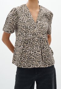 Blusa a maniche corte con stampa leopardata, scollatura a V profonda, vita peplum e tessuto testurizzato. Abbinata a pantaloni neri a vita alta.