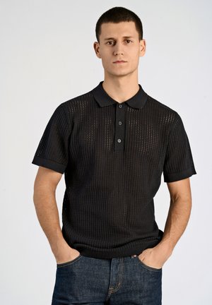 Polo shirt nera a maglia con maniche corte, caratterizzata da un motivo testurizzato e una chiusura a tre bottoni. Abbinata a jeans in denim scuri.