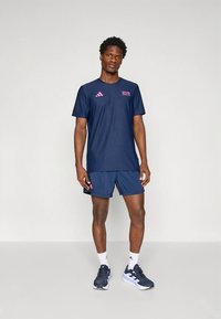 Tengerészkék sportfelszerelés, amely rövid ujjú ingből és rövidnadrágból áll. Rózsaszín logó részletekkel, kényelmes szabással és könnyű anyagból készült.