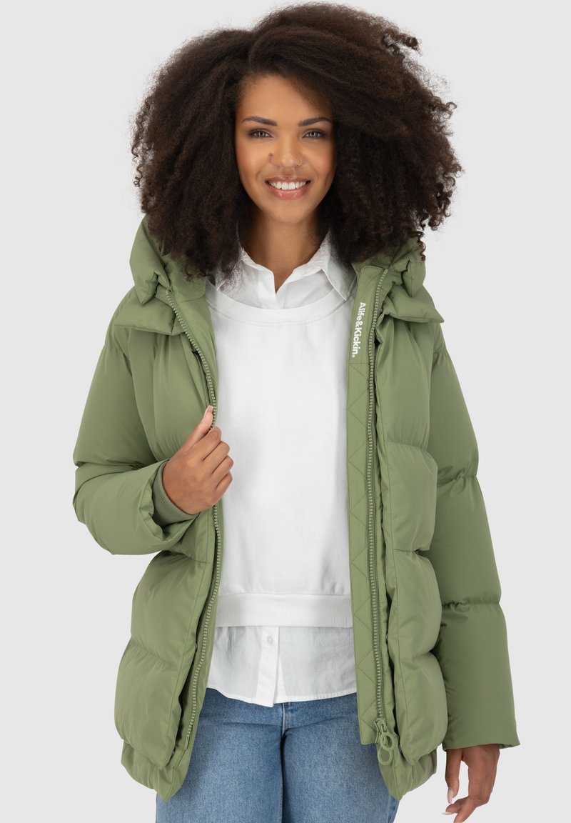 Giacca a vento verde con cappuccio, caratterizzata da un design trapuntato e chiusura frontale con zip. Abbinata a una camicia bianca, per un look casual. Tessuto morbido.