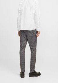 Grå rutiga byxor med en avsmalnande passform, tillverkade av ett texturerat tyg. Bärs med en vit skjorta och svarta skor.