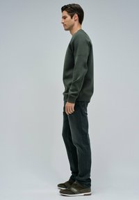 Felpa verde scuro con accenti a coste sulle spalle, abbinata a jeans scuri e sneakers verdi. Tessuto morbido e vestibilità rilassata.