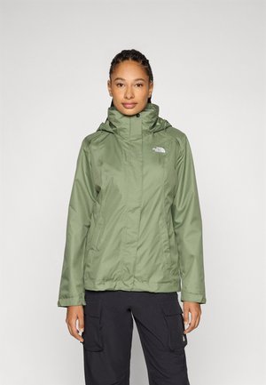 Veste imperméable verte avec un col haut et une capuche ajustable. Comprend des poches zippées et un logo sur la poitrine gauche. Tissu lisse et léger.