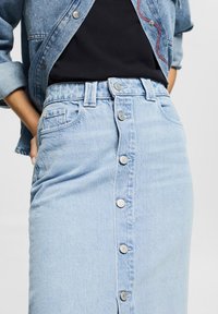 Vaaleansininen farkkuhame korkean vyötärön kanssa, jossa on etupainike, kaksi sivutaskua ja hienovaraiset kulutukset kankaassa.