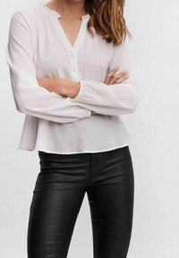 Weißes, strukturiertes Bluse mit Knopfleiste und Mandarin-Kragen, kombiniert mit figurbetonten schwarzen Lederhosen. Lange, sanft gepuffte Ärmel.